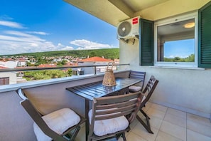 A balcony with a table and chairs, an air conditioning unit, and a view of a town.