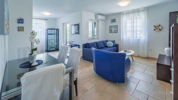 A modern living area with a dining table, blue sofa, and a small round table. - Apartment Jelena Punat | 300m from Beach & near Medane Beach (Punat)