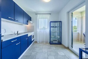 Una cocina moderna con armarios azules, una encimera blanca y un ventanal que da a un balcón.