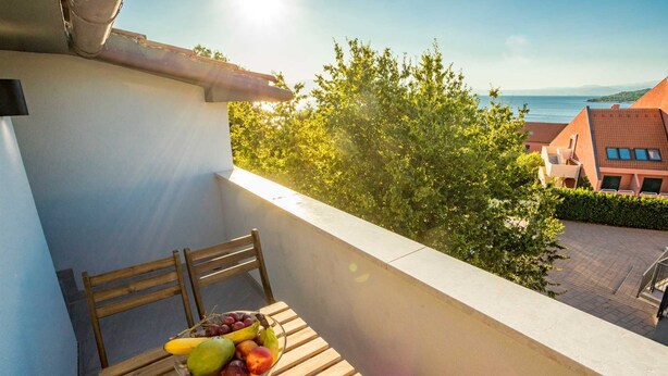 A balcony with a wooden chair and a bowl of fruit.