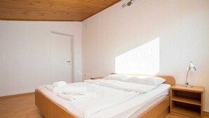 A bedroom with a wooden bed, white linens, a nightstand with a lamp, and a door.
