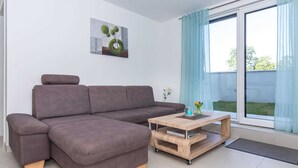 Un salon moderne avec un canapé d’angle gris, une table basse en bois et une grande fenêtre ornée de rideaux bleus.