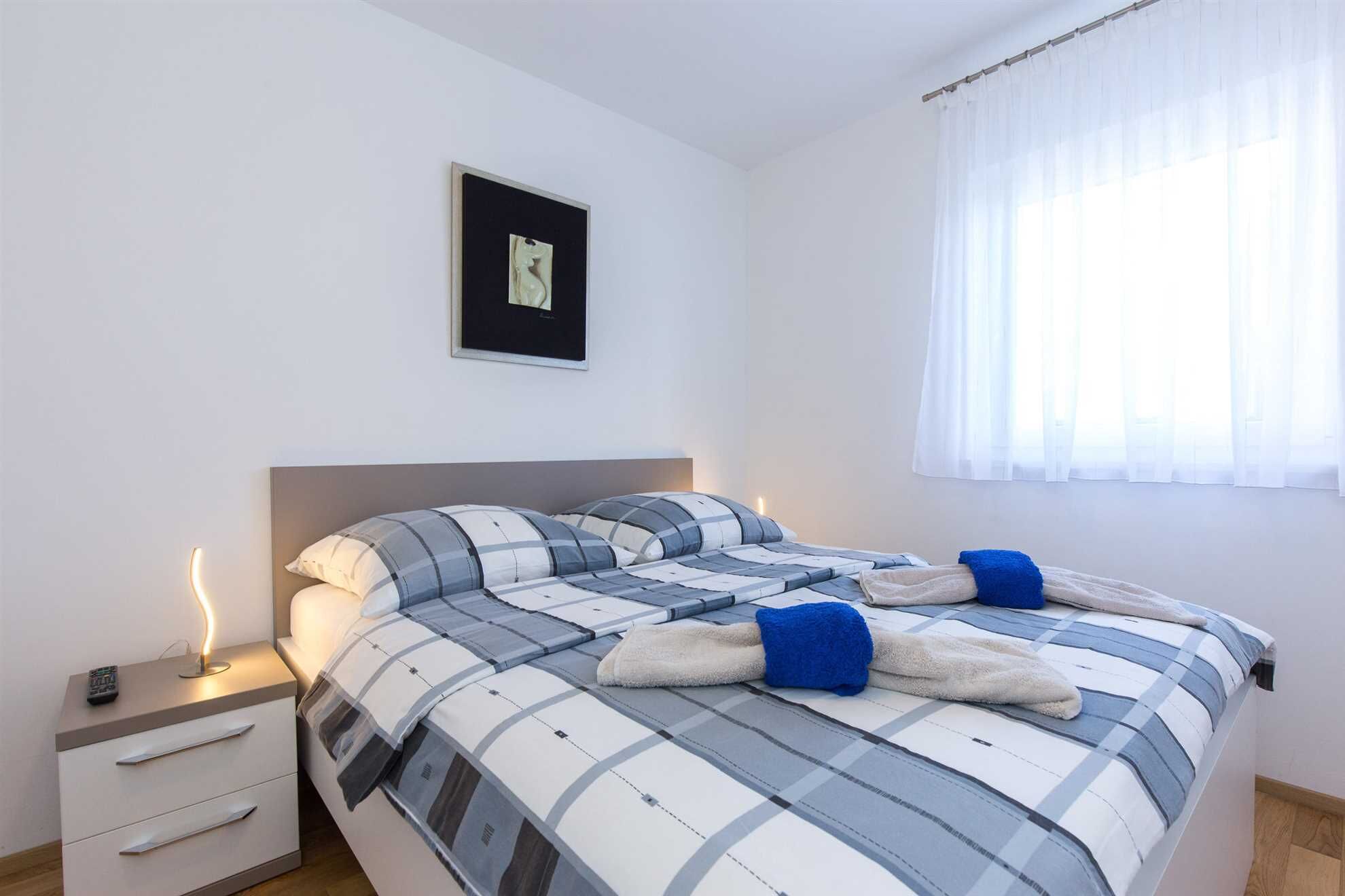Un letto rifatto con cura, una coperta a quadri, un comodino con un telecomando e un quadro appeso alla parete.