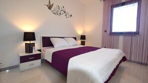 A modern bedroom with a large bed, two bedside tables with lamps, a decorative wall piece, and a window with curtains.