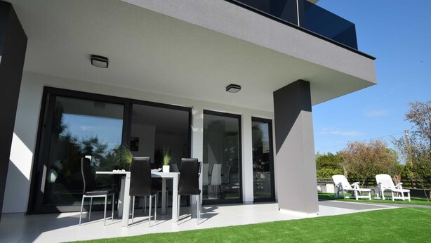 A modern two-story house with a balcony, large sliding glass doors, and a well-maintained lawn.