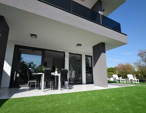 Una casa moderna a due piani con un balcone, ampie porte scorrevoli in vetro e un prato curato.