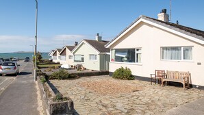 A row of coastal houses with a paved driveway, a bench, and a street lamp. - Marimar : Charming 3‑Bed Pet-Friendly Bungalow Steps from Rhosneigr Beach | Managed by Anglesey Holi (Rhosneigr)