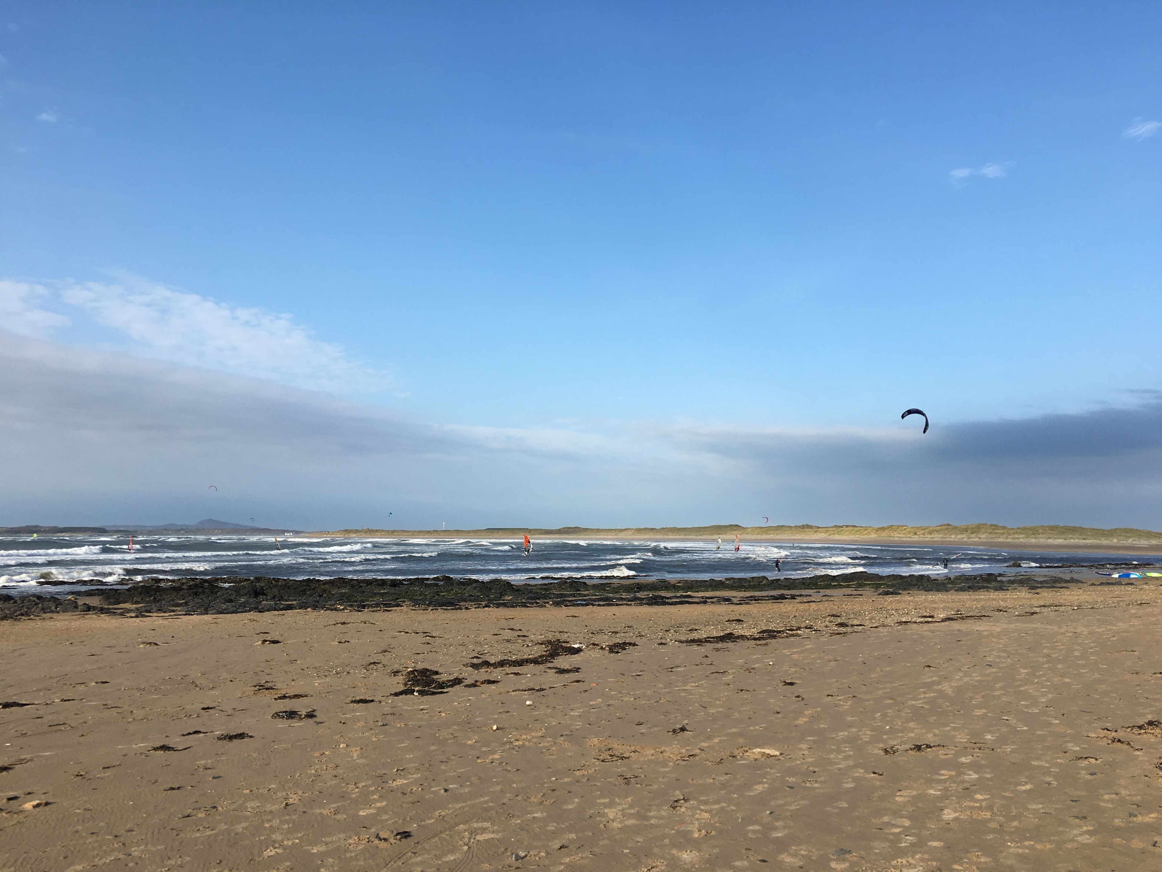En strand med klart himmel, bølger og en fjerndunet.