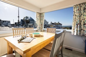 Ein Essbereich mit Holztisch, Stühlen und Blick auf das Meer und Häuser.