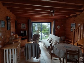 A wooden cabin interior with a sofa, a table, a fan, a television, and a view of the outdoors.