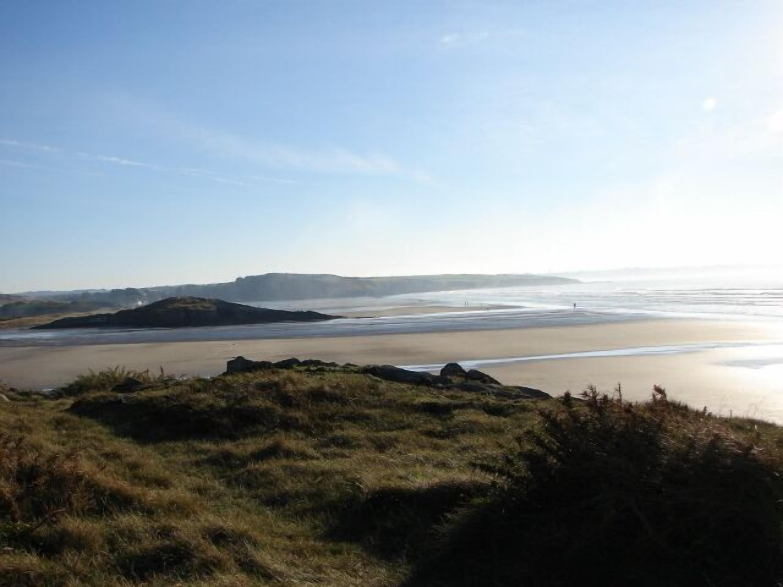 A coastal landscape with a beach, grassy areas, and distant hills.