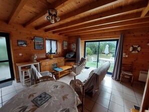 L’intérieur d’un chalet en bois comprend une table à manger, des chaises, un canapé, un téléviseur et offre une vue sur l’extérieur.