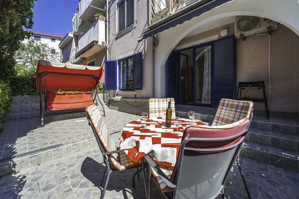 An outdoor seating area with a table set for two, a chair, and a covered seating area.
