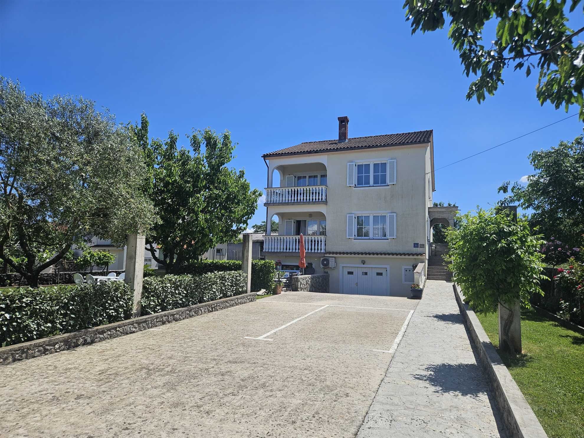 A two-story building with a balcony, a garage, and a paved driveway.