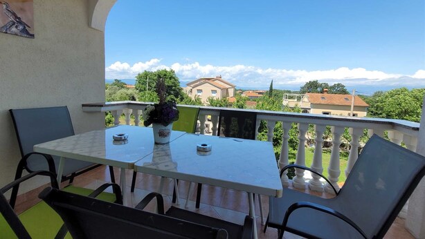Ein Balkon mit Tisch und Stühlen, einem Blumenstrauß und Blick auf Häuser und Bäume.