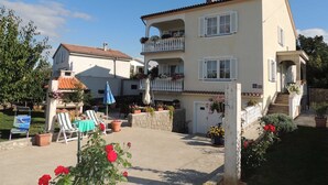 Ein zweistöckiges Gebäude mit Balkon, Sitzgelegenheiten im Freien und Blumentöpfen.
