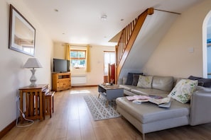 A modern living room with a sofa, a television, a wooden cabinet, and a staircase. - The Granary: A two bed, pet-friendly holiday cottage (Ty Croes)