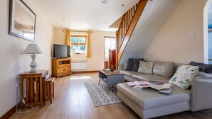 A modern living room with a sofa, a TV, wooden furniture, and a staircase.