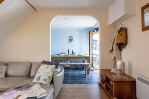 A cozy living room with a sofa, a coffee table with magazines, a dining area with a table and chairs, and a kitchen visible through an archway.