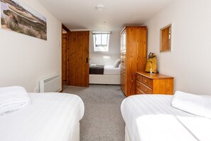 A bedroom with two beds, a wooden wardrobe, a radiator, and a skylight. - The Granary: A two bed, pet-friendly holiday cottage (Ty Croes)