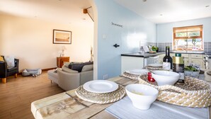 A modern kitchen with a dining area, featuring a wooden table set with plates and bowls, a bottle of wine, and a basket of bread.