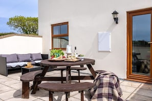 An outdoor patio with a round wooden table, a sofa, and a bench. - The Granary: A two bed, pet-friendly holiday cottage (Ty Croes)