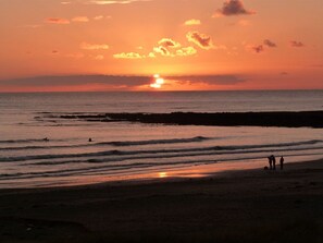 A sunset over a beach with waves, a few people on the sand, and a clear sky. - The Granary: A two bed, pet-friendly holiday cottage (Ty Croes)
