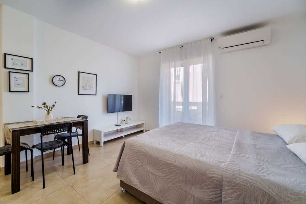 Un dormitorio con cama, un escritorio con silla, televisor y ventana con cortinas.