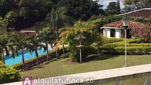 A pool area with palm trees, a gazebo, and a building with a tiled roof. - Villa for rent in Cerritos Pereira (Pereira)