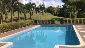 A rectangular swimming pool with a clear blue water surface, surrounded by a low hedge and palm trees. - Villa for rent in Cerritos Pereira (Pereira)