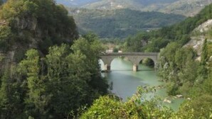 Un puente sobre un río rodeado de vegetación exuberante y colinas.