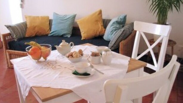 Una mesa de comedor con mantel blanco, un cuenco de fruta, una tetera, tazas y un plato de galletas.