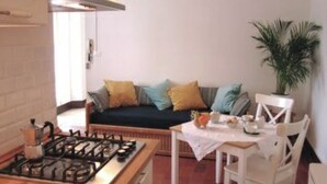 Cocina compacta con estufa a gas, mesa de comedor con sillas y sofá con cojines.