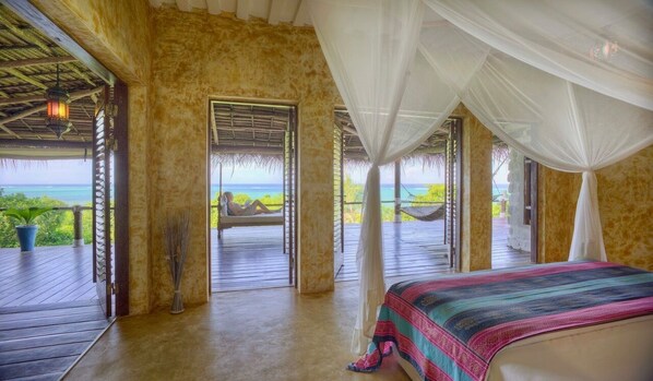 A bedroom with a bed, a window with a view of the sea, and a balcony with a hammock.