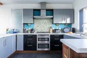 A modern kitchen with black cabinets, a tiled backsplash, stainless steel appliances, and a built-in oven. - The View: A modern beach retreat for 8 guests on Anglesey (Rhosneigr)