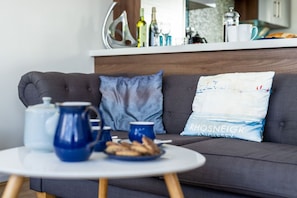 A living room with a grey sofa, a round white table, and a blue mug on the table. - The View: A modern beach retreat for 8 guests on Anglesey (Rhosneigr)