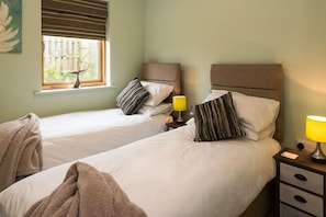A hotel room with two beds, a window with a view of a fence, and bedside lamps.