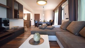 En moderne stue med en sofa, et sofabord med en dekorativ vase, et fjernsyn og et spiseområde i baggrunden.