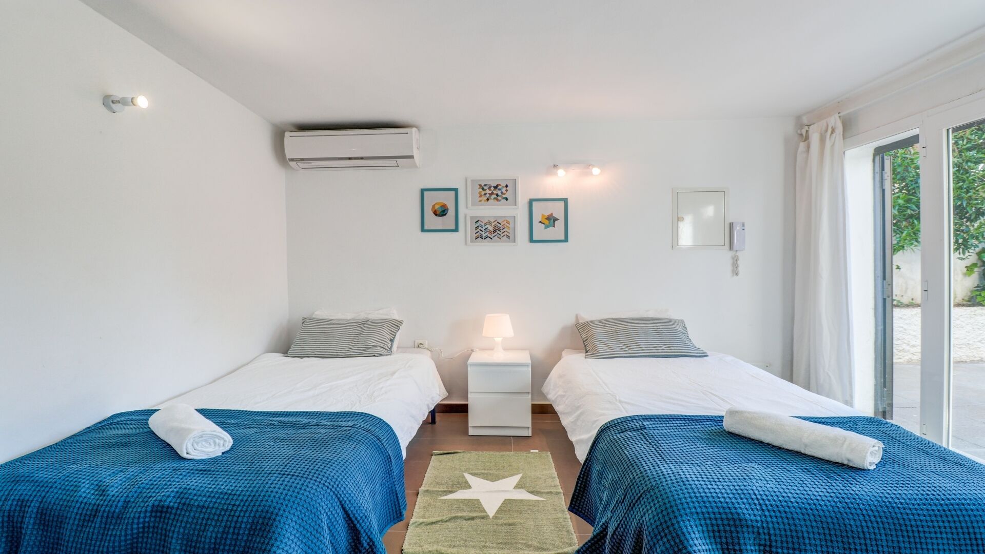 Een kamer met twee bedden, een nachtkastje, een lamp, wanddecoratie en een airconditioning.
