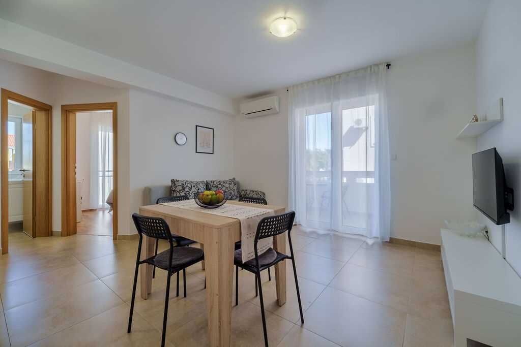 Un comedor con una mesa de madera, cuatro sillas y un bol de fruta. Un televisor sobre un mueble se encuentra a la derecha.