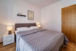 A bedroom with a bed, bedside tables, a wooden door, and a wall-mounted shelf with a framed picture. - Apartment Nino 3 on the first floor (Malinska)