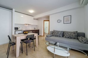 Ein moderner Wohnraum mit Essbereich, Küchenzeile und einer Couch mit gemusterten Kissen.