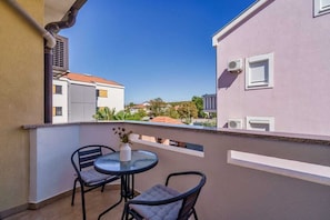 A balcony with two chairs and a table, overlooking a residential area with buildings and trees. - Apartment Nino 3 on the first floor (Malinska)