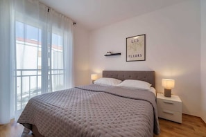 Ein Schlafzimmer mit einem Bett, zwei Nachttischen mit Lampen, einem Fenster mit Vorhängen und einem Wandbild.
