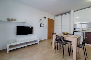 A modern living room with a flat-screen TV, a dining table with chairs, a white bench, and a kitchen area with cabinets and appliances. - Apartment Nino 3 on the first floor (Malinska)