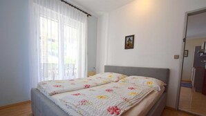 A bedroom with a bed, a window with sheer curtains, a small picture on the wall, and a door leading to another room.