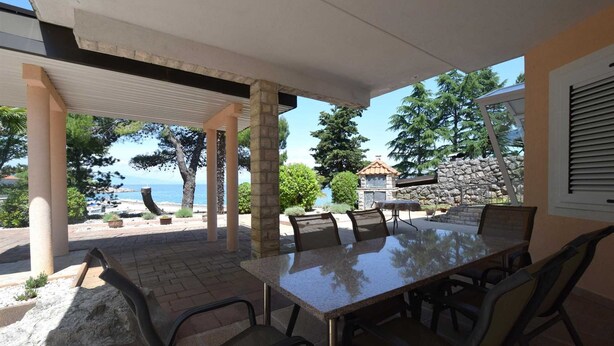 An outdoor patio with a table and chairs, overlooking a scenic view of the sea and trees.