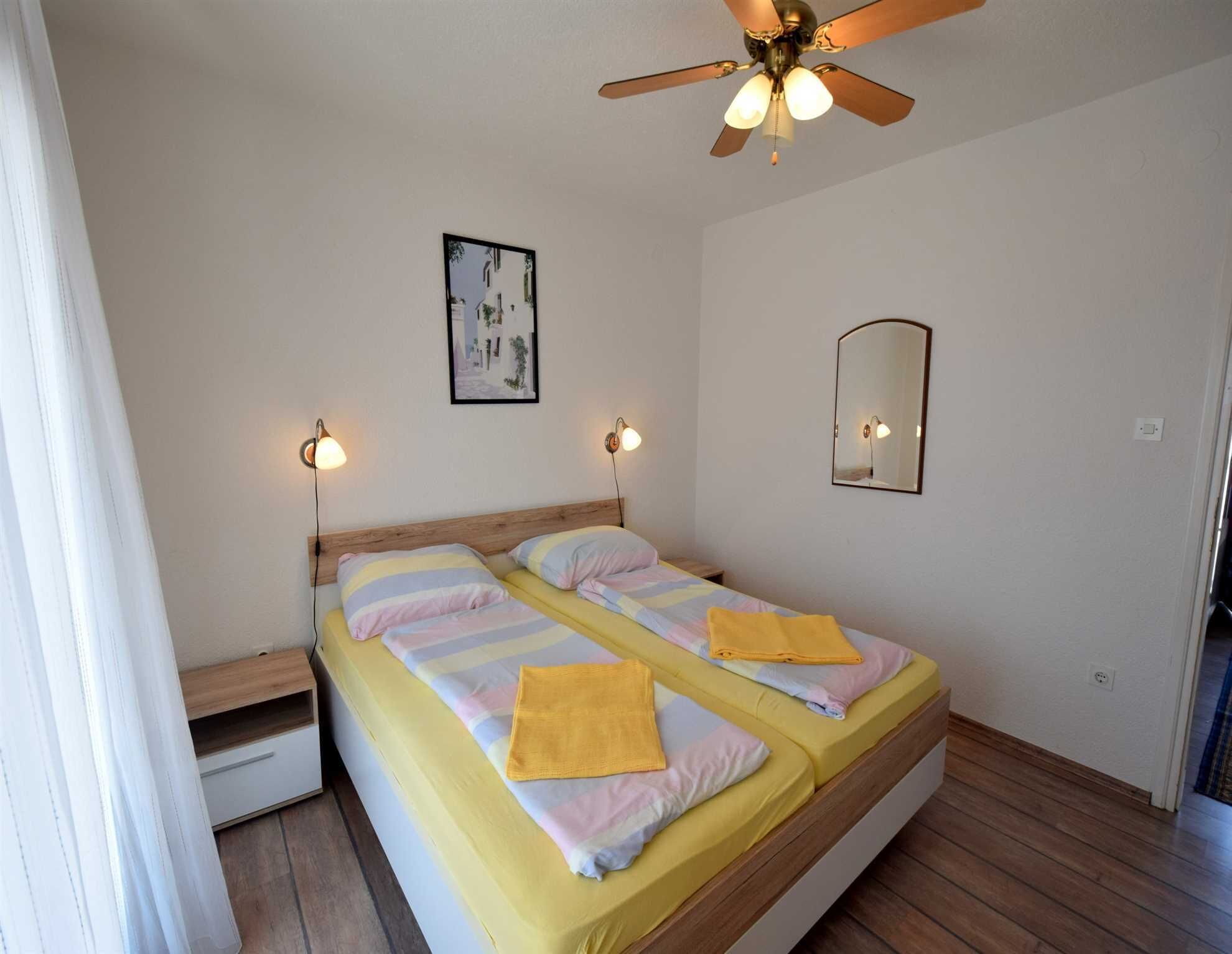Un letto matrimoniale con testiera in legno, due lampade sui comodini, una ventola a soffitto, un quadro incorniciato e uno specchio appeso al muro.