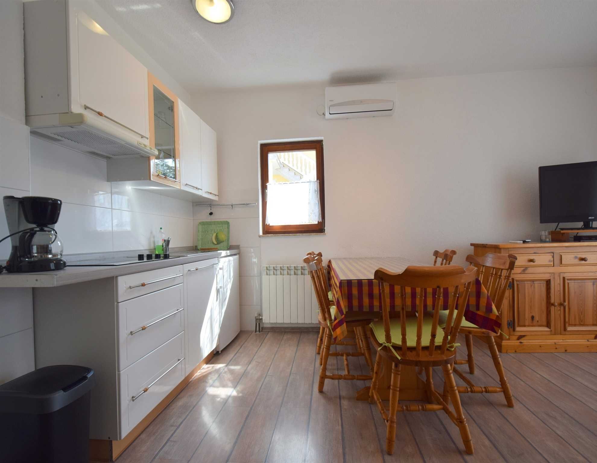 Une cuisine compacte avec des meubles blancs, une machine à café, un radiateur et un coin repas comprenant des chaises et une table en bois.