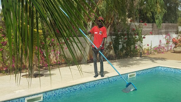 Una persona limpiando una piscina con un utensilio de mango largo.